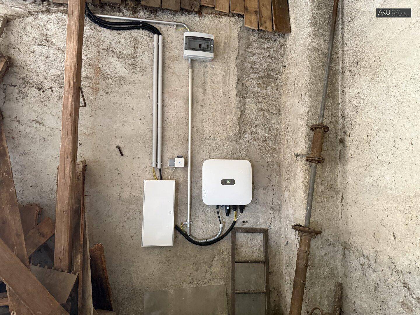Elektrische Installationen mit Sicherungskasten und Wechselrichter an einer rauen Wand in einem Funktionsraum.