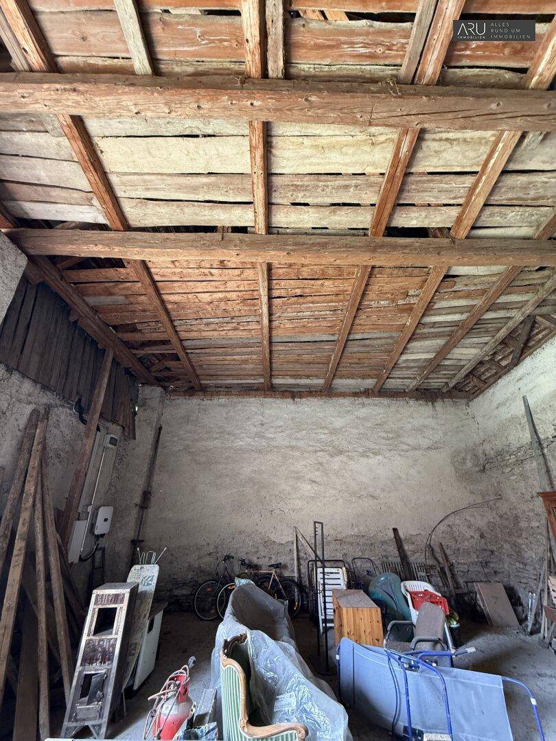 Alter, unfertiger Raum mit sichtbaren Holzbalken an der Decke und verschiedenen gelagerten Gegenständen.