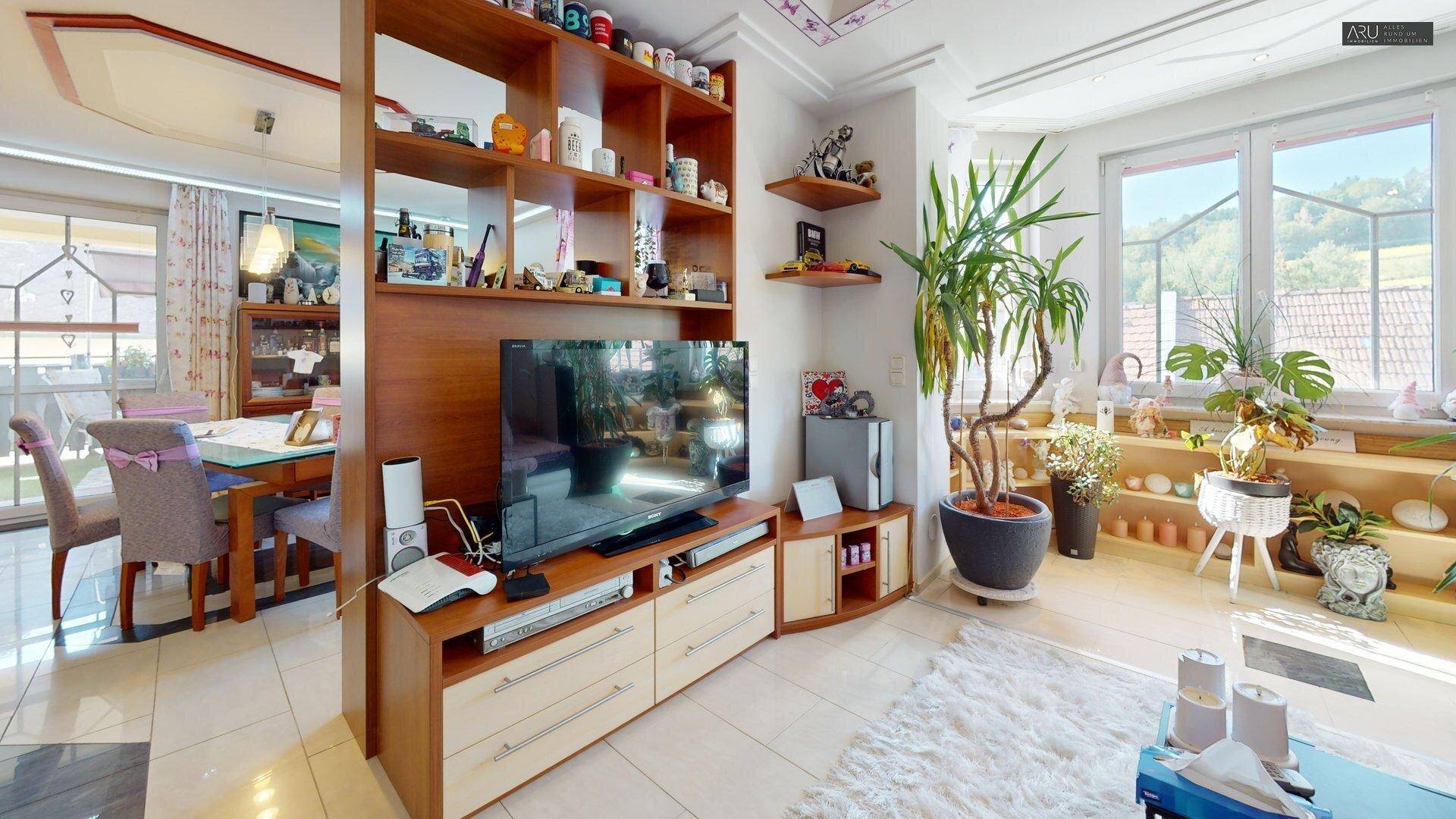 Gemütlicher Wohnbereich mit Fernseher, vielen Pflanzen und Blick ins Grüne.