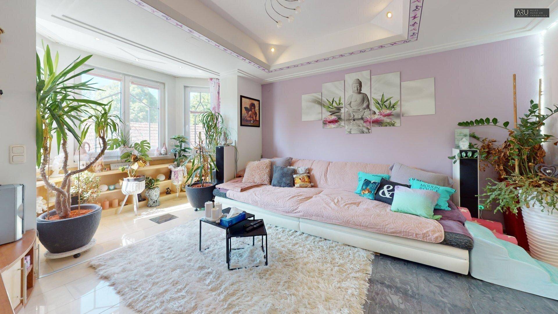 Geräumiges Wohnzimmer mit großem Sofa, vielen Pflanzen und dekorativer Decke.