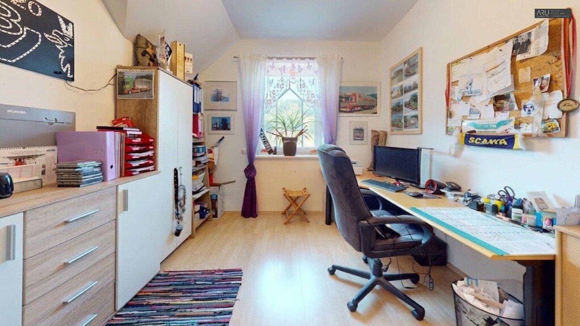 Helles Arbeitszimmer mit Schreibtisch, Regalen und Laminatboden.