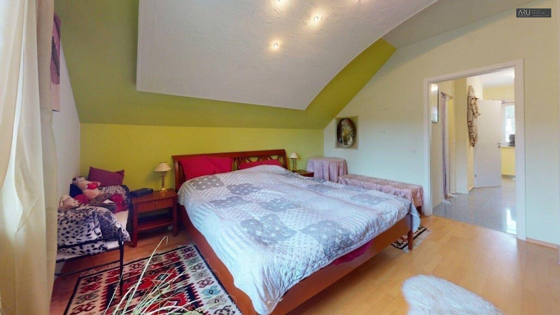 Helles Schlafzimmer mit Doppelbett, Dachschräge und Holzboden.
