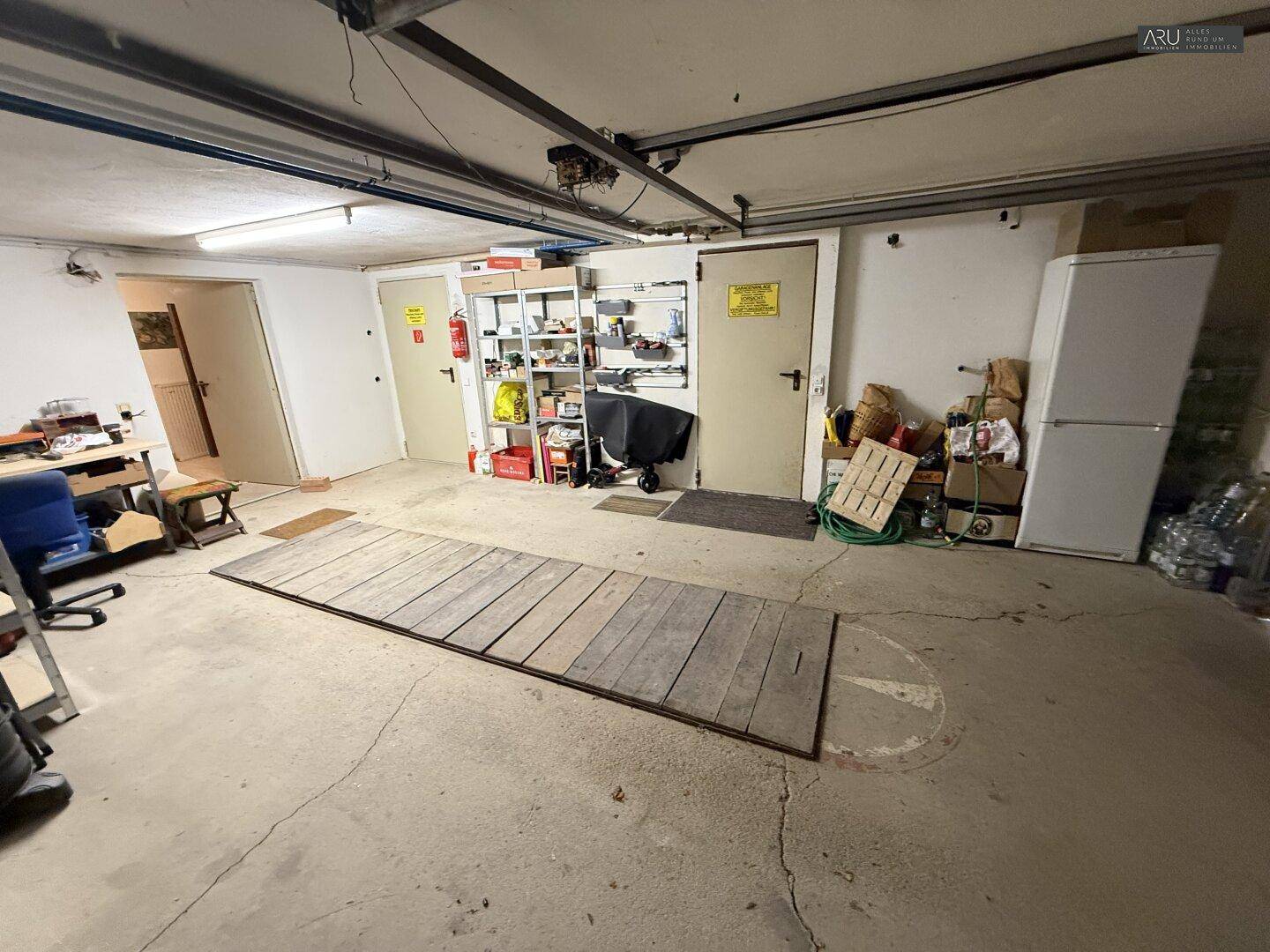 Geräumige Garage mit Betonboden, Stauraum und Zugang zu weiteren Räumen.