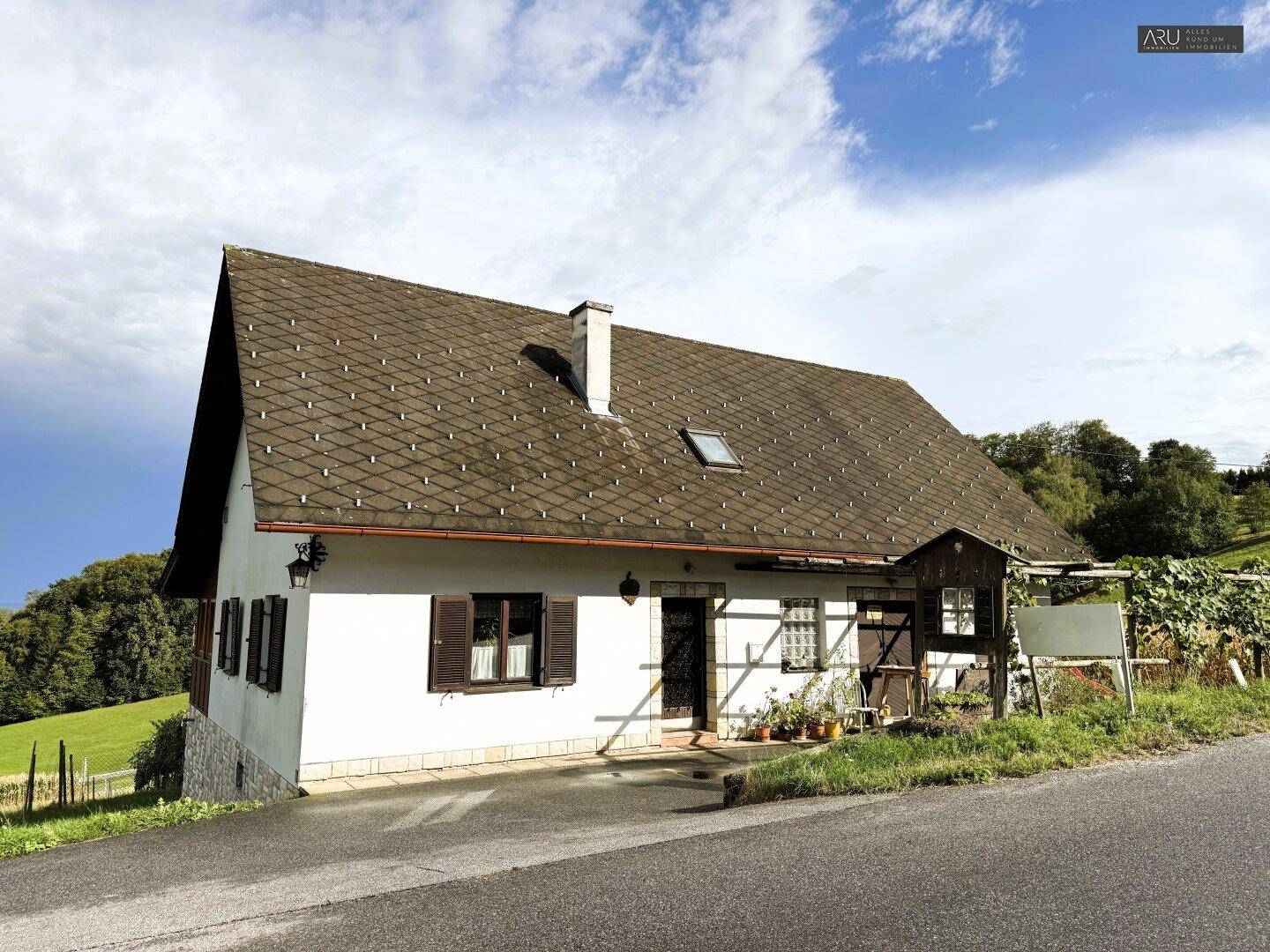 Charmantes Landhaus mit Satteldach und braunen Fensterläden, umgeben von ländlicher Idylle.