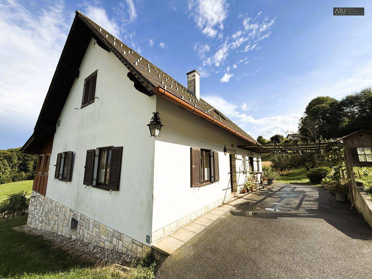 Traditionelles Landhaus mit weißer Fassade und Satteldach, umgeben von grüner Natur.