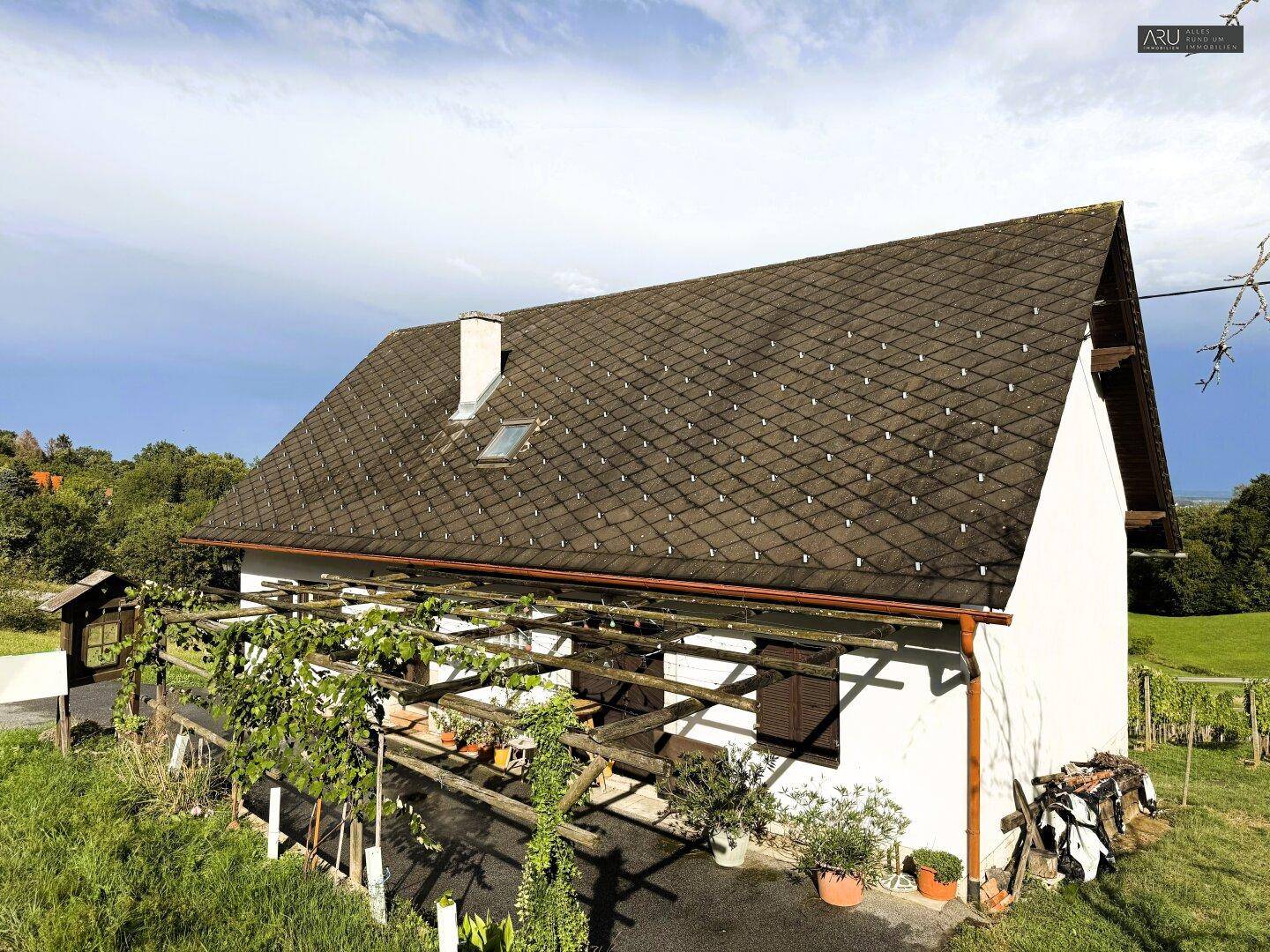 Traditionelles Landhaus mit Satteldach und überdachtem Eingangsbereich, umgeben von Grün.