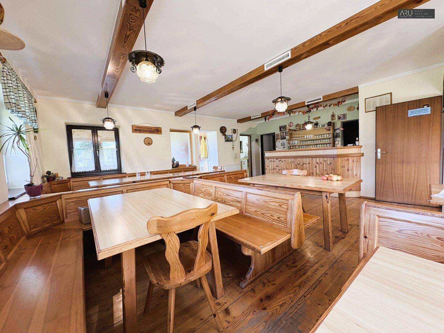 Rustikaler Essbereich mit Holztischen, Bänken und sichtbaren Deckenbalken, ideal für gesellige Runden.