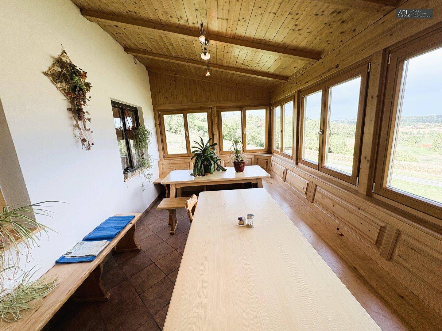 Heller Wintergarten mit Holzverkleidung und großen Fenstern, bietet weite Ausblicke auf die Landschaft.