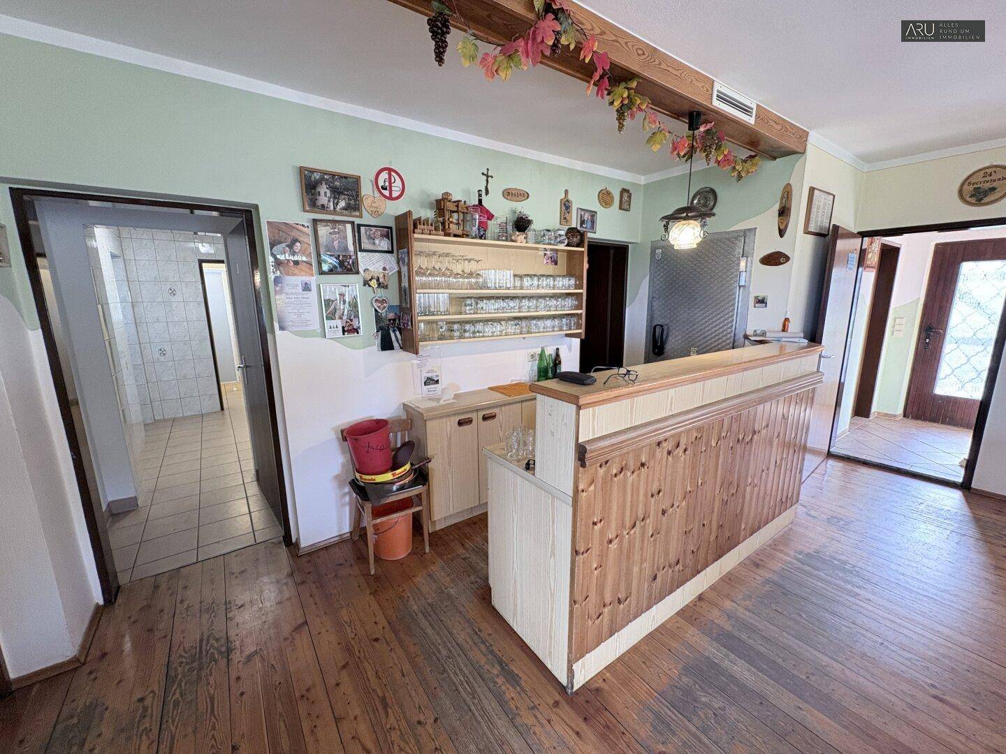 Traditionelle Bar mit Holzverkleidung und Gläserregal, angrenzend an weitere Räume.