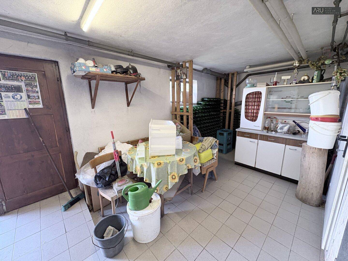 Kellerraum mit gefliestem Boden, Tisch und Schrank, genutzt als Lager- und Arbeitsbereich.