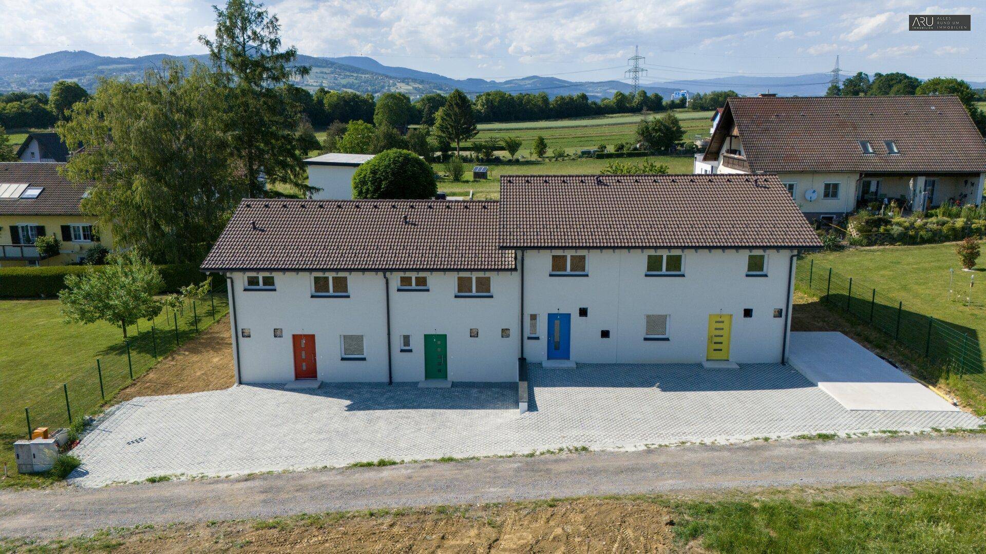 Luftaufnahme der Reihenhäuser mit weitem Blick auf die umliegende grüne Landschaft und Berge.