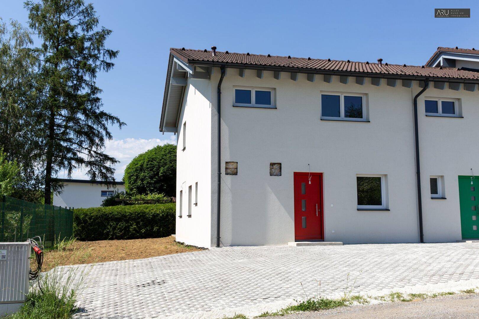 Nahaufnahme eines modernen Reihenhauses mit roter Eingangstür und gepflasterter Zufahrt.