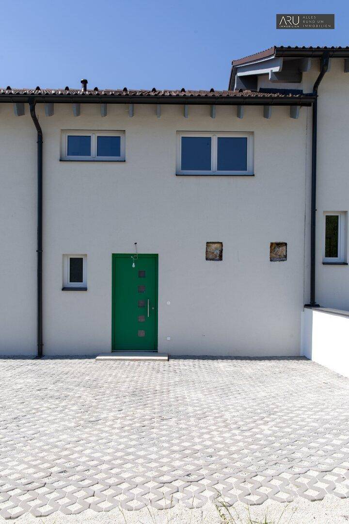 Nahaufnahme der modernen Fassade eines Reihenhauses mit grüner Eingangstür und gepflastertem Vorplatz.
