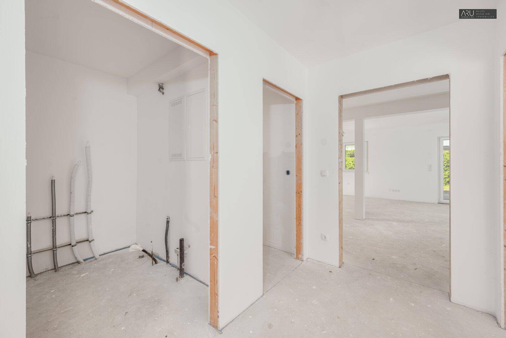 Unfertiger Flurbereich mit Betonboden und Zugängen zu verschiedenen Räumen, inklusive Sanitärinstallationen.