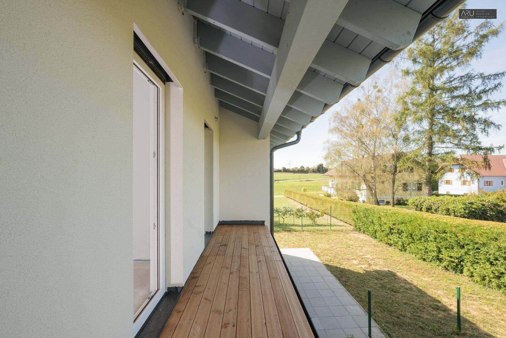 Langer Holzbalkon mit Blick auf den Garten und die umliegende grüne Landschaft.