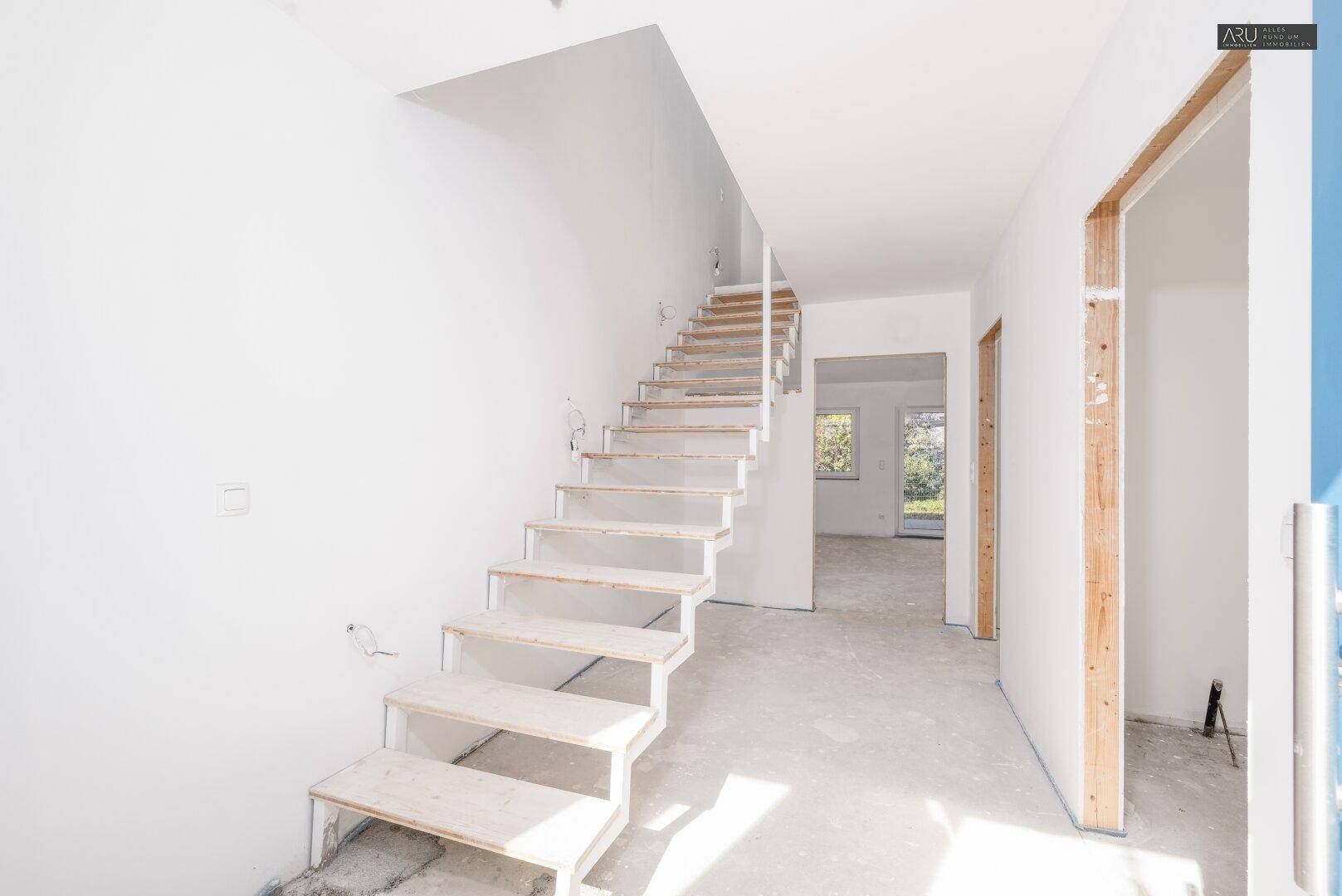 Heller Flur im Rohbau mit moderner offener Treppe und viel Tageslicht.