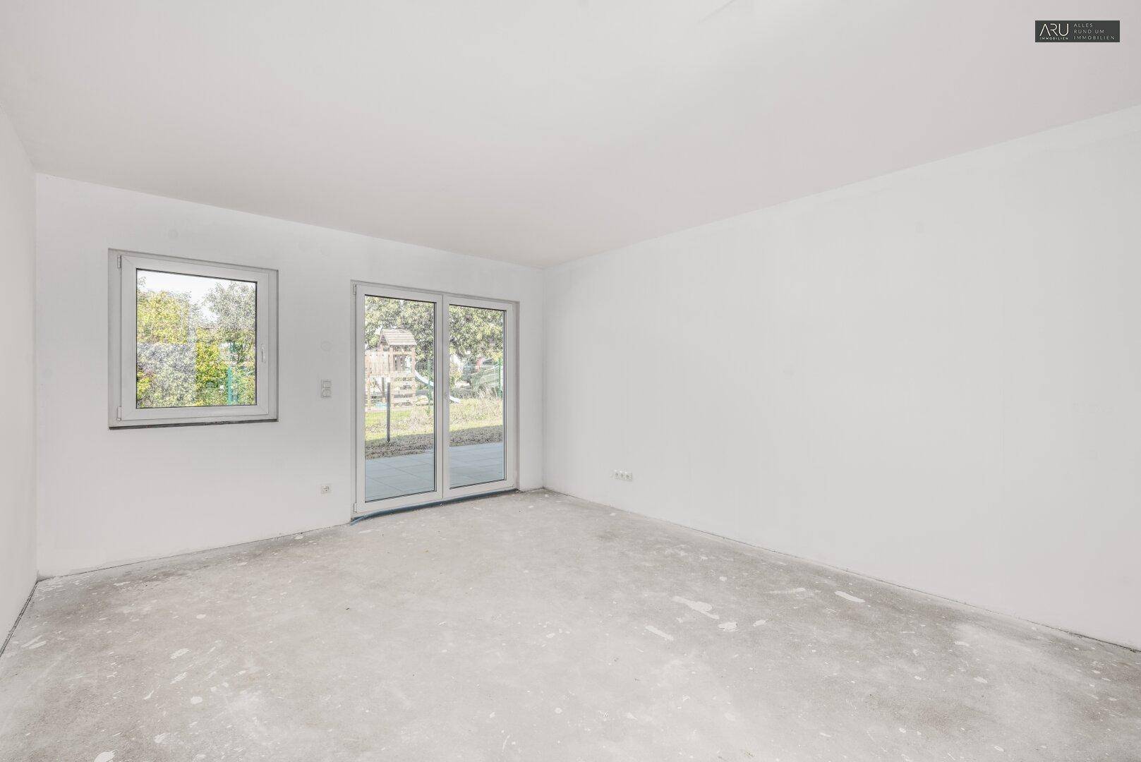 Unfertiger Wohnraum mit großen Schiebetüren zum Garten und viel natürlichem Licht.