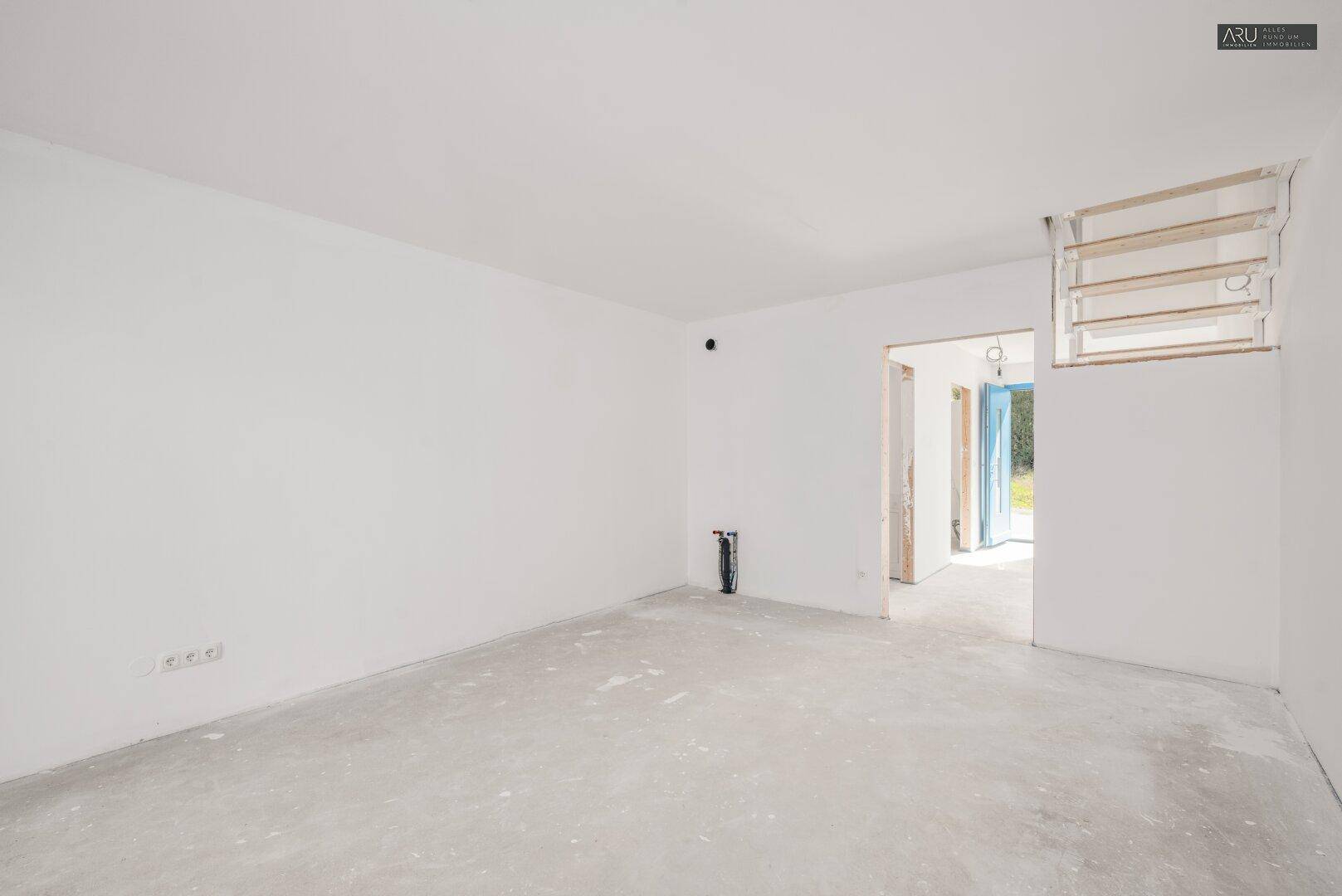 Heller, unfertiger Raum mit weißen Wänden und Betonboden, bereit für den Ausbau.