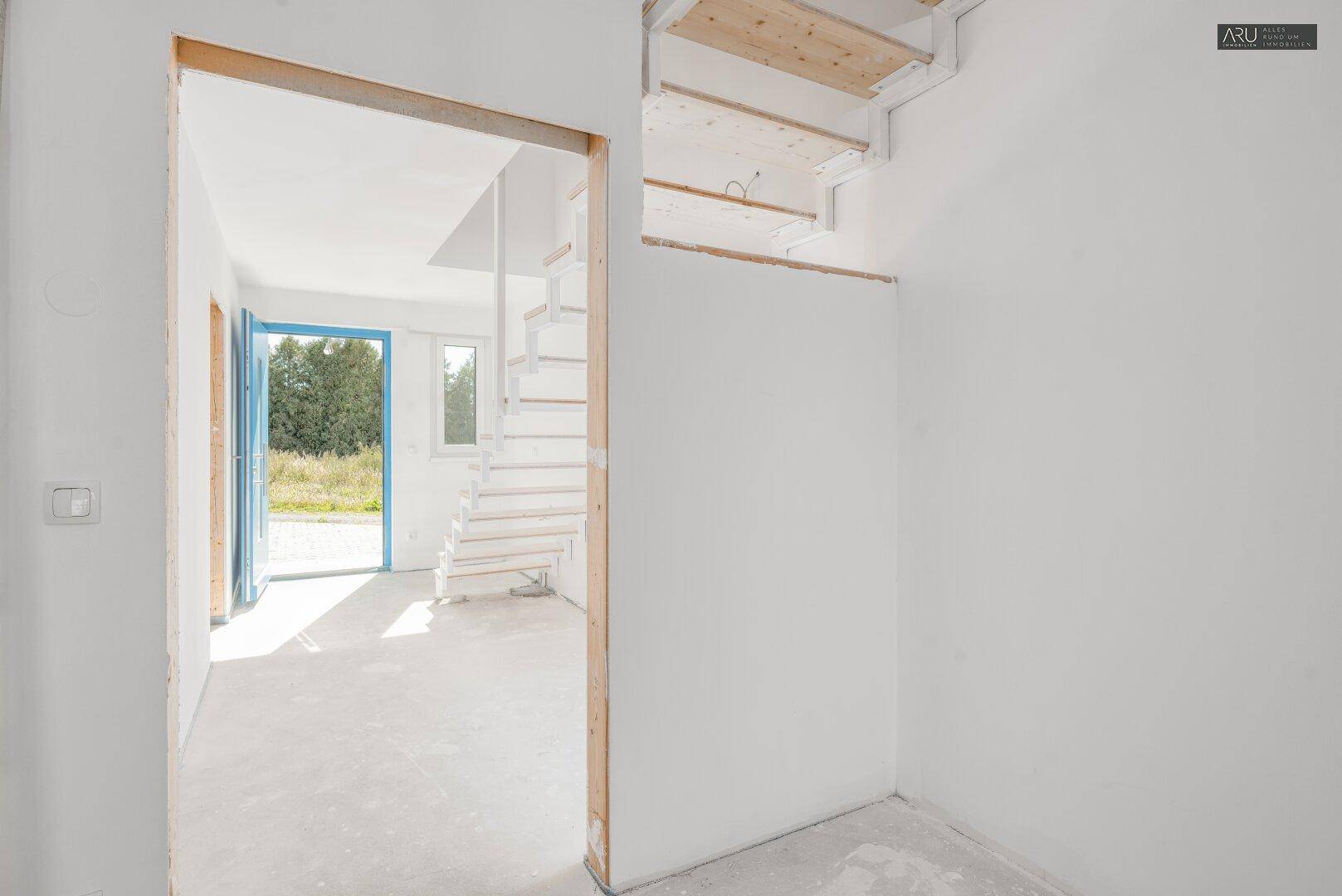 Eingangsbereich im Rohbau mit Blick auf die offene Treppe und den Garten.
