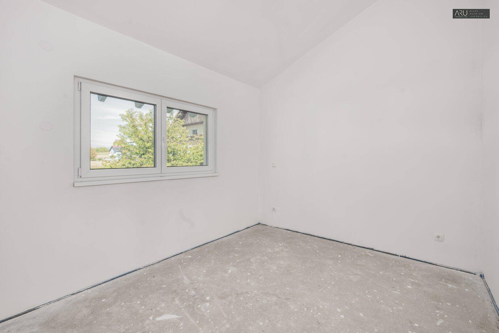 Helles, unfertiges Schlafzimmer mit Fenster und Blick auf die umliegende Natur.