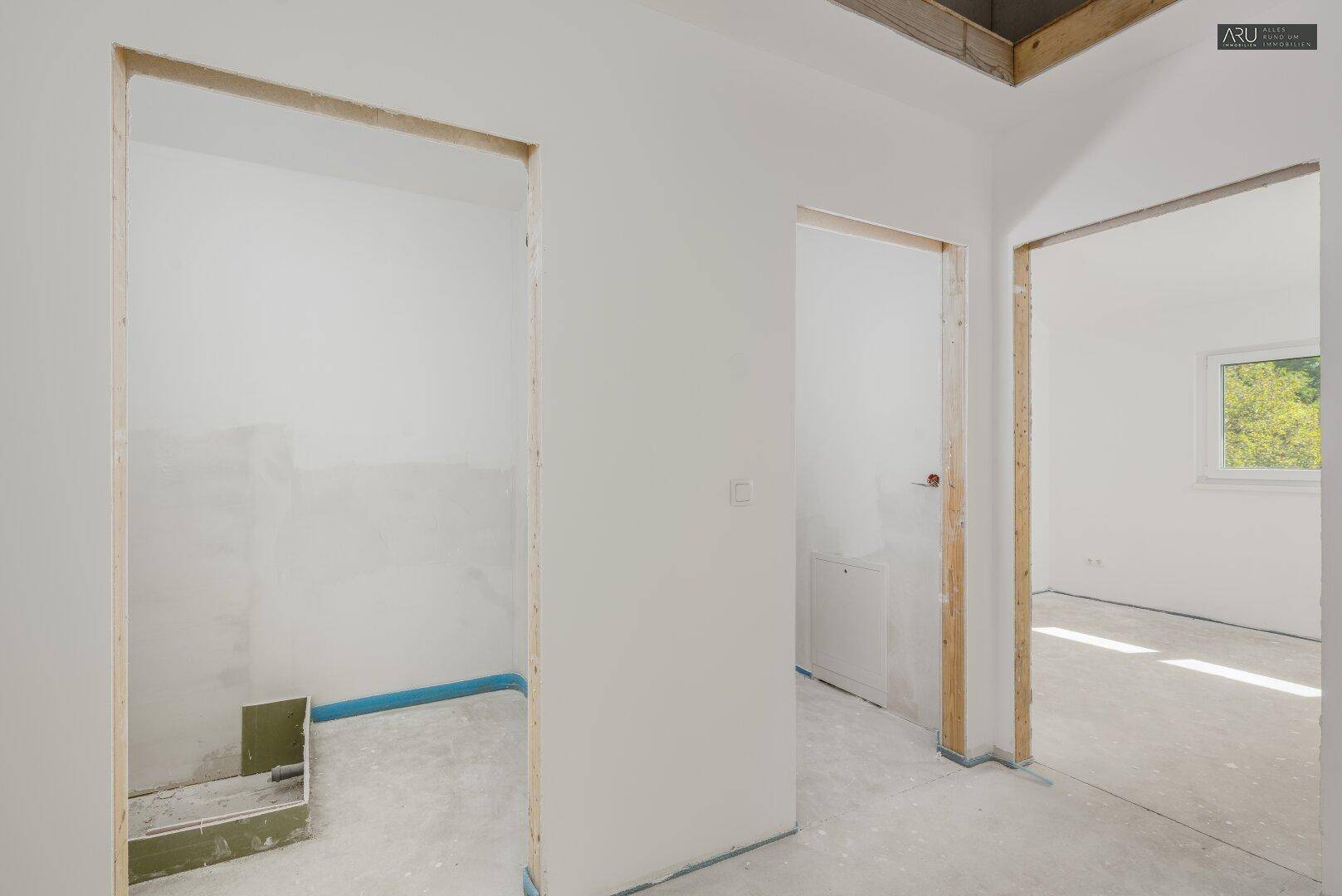 Flur im Rohbau mit Zugängen zu verschiedenen Räumen, darunter ein Badezimmer.
