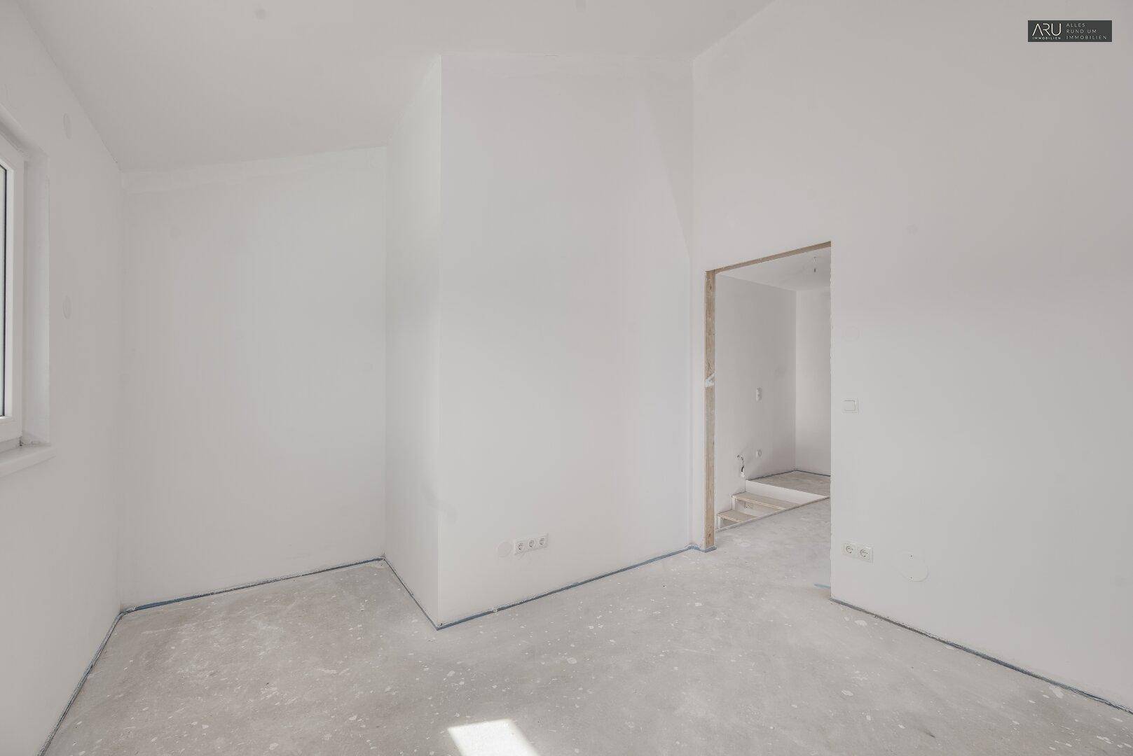 Helles, unfertiges Zimmer mit weißen Wänden und Betonboden, ideal als Schlaf- oder Arbeitszimmer.