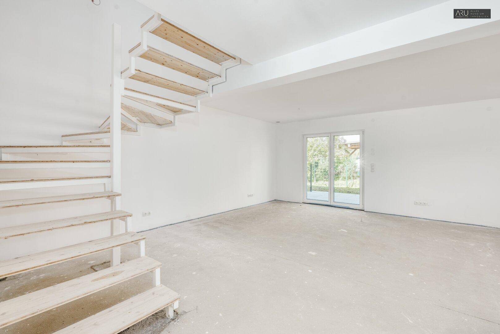 Heller, unfertiger Wohnbereich mit offener Holztreppe und Zugang zur Terrasse.
