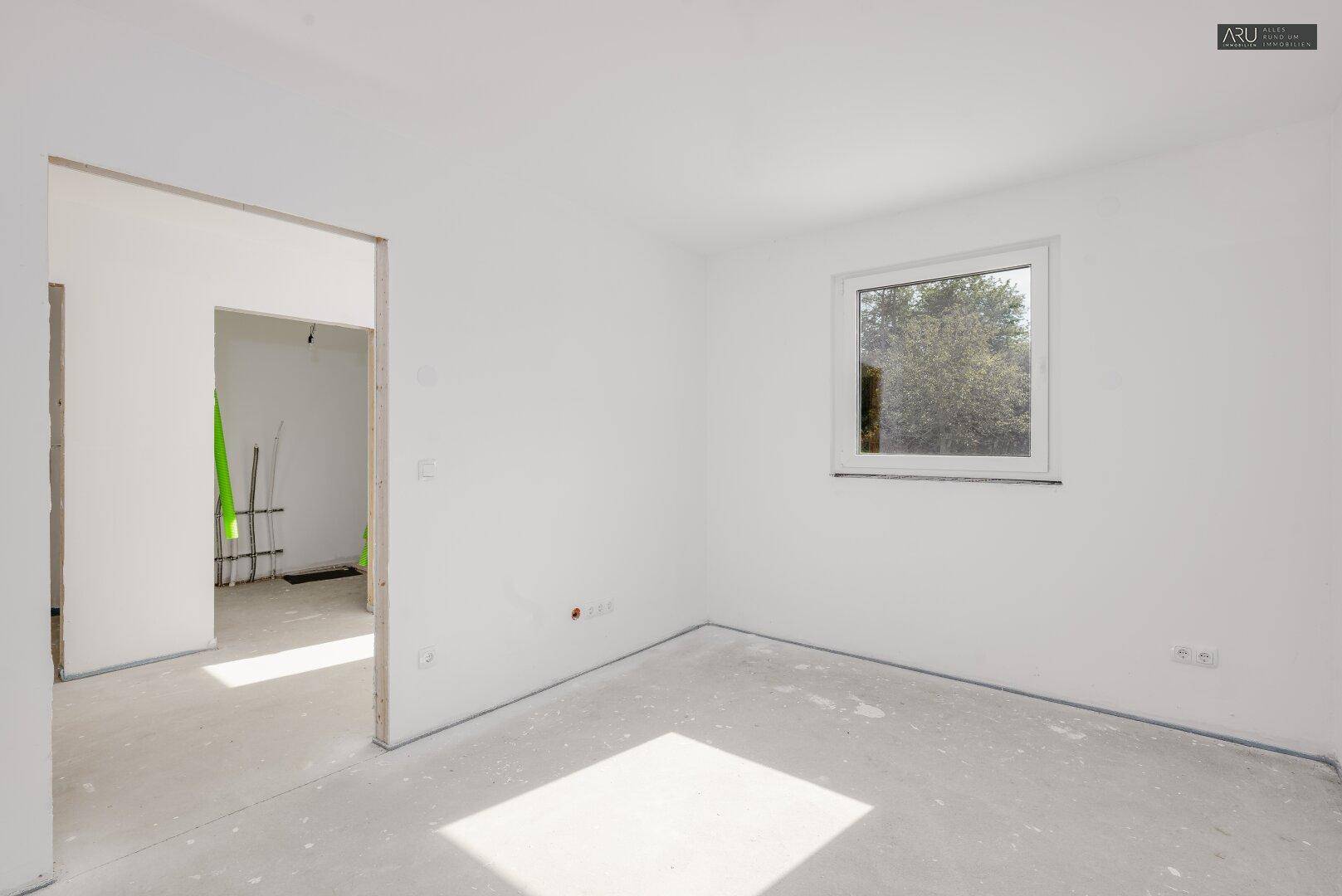 Unfertiger Raum im Erdgeschoss mit einem Fenster und viel Tageslicht.