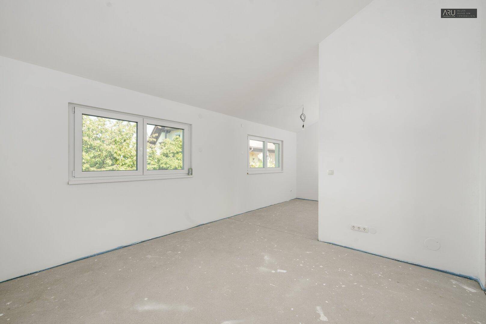 Helles Schlafzimmer im Rohbau mit zwei Fenstern und leichter Dachschräge.