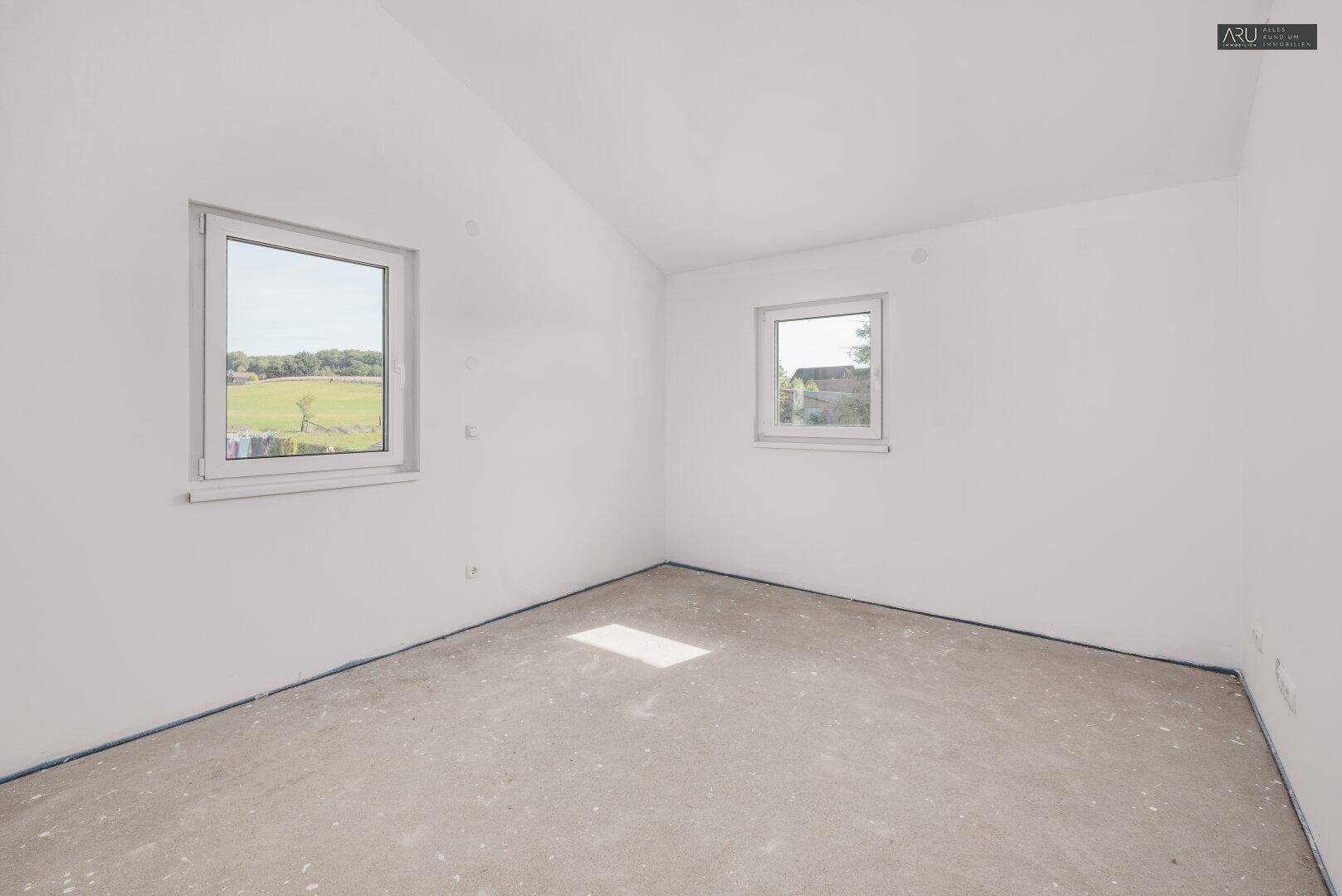 Helles Schlafzimmer im Rohbau mit zwei Fenstern und leichter Dachschräge.