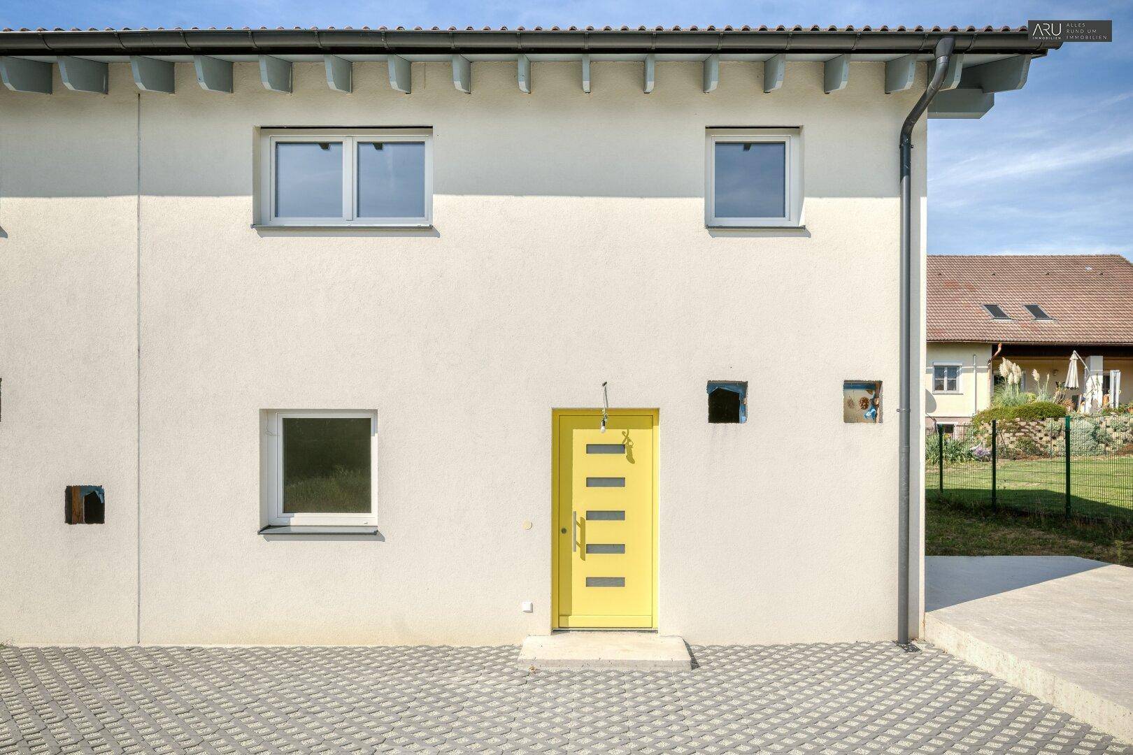 Nahaufnahme der modernen Fassade eines Reihenhauses mit gelber Eingangstür und Fenstern.