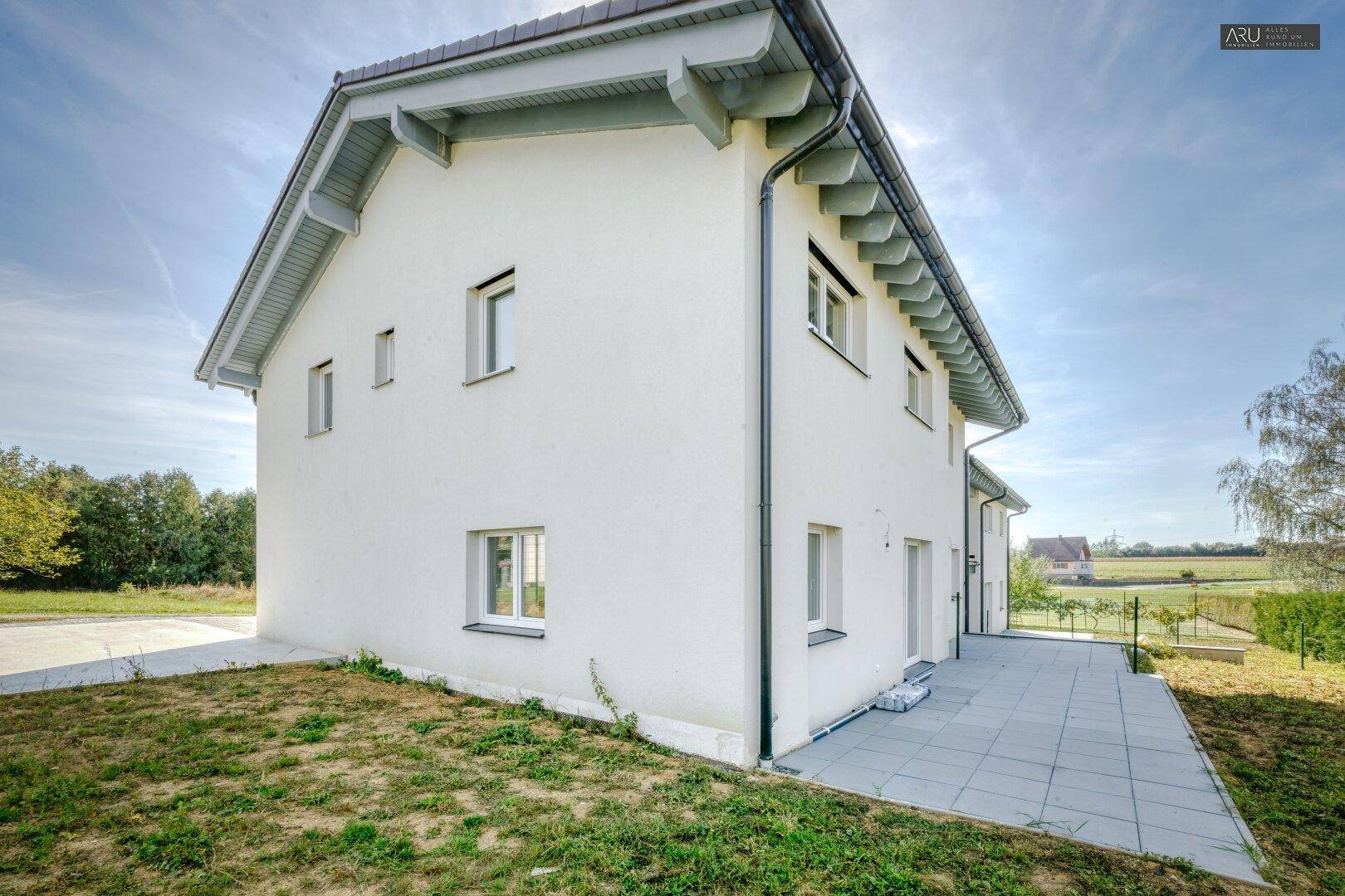Seitenansicht des Reihenhauses mit kleiner Rasenfläche und gepflasterter Terrasse.