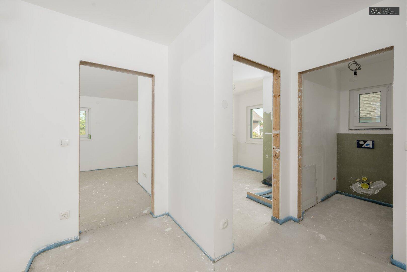 Flur im Rohbau mit Zugängen zu unfertigen Räumen, darunter ein potenzielles Badezimmer.