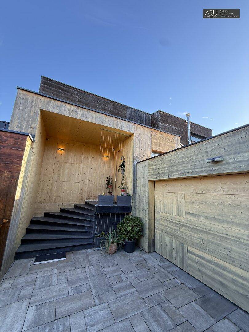 Eingangsbereich des modernen Holzhauses mit Außentreppe und integrierter Garage.