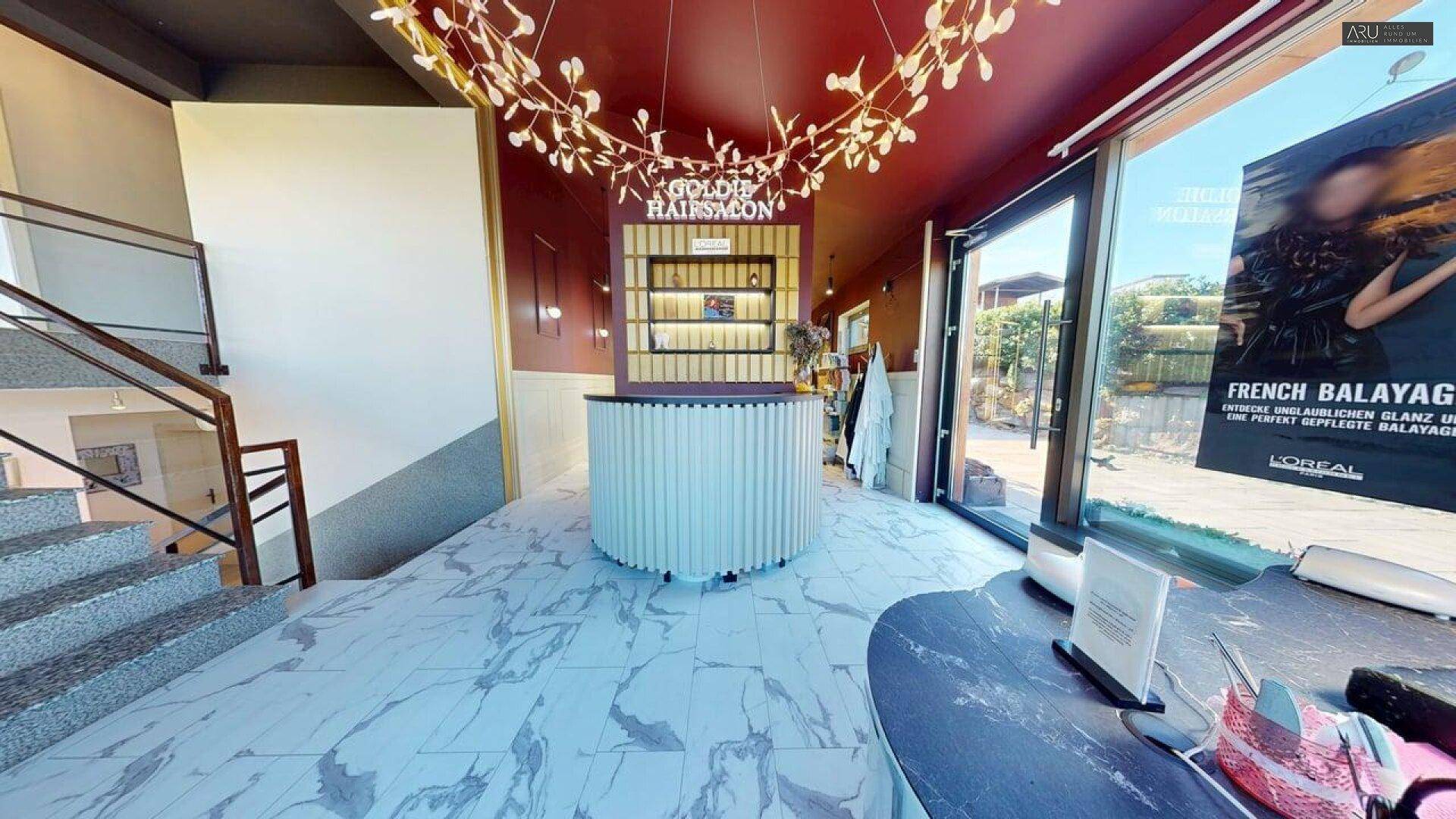 Empfangsbereich eines modernen Salons mit Marmorboden, Designleuchte und Treppenaufgang.