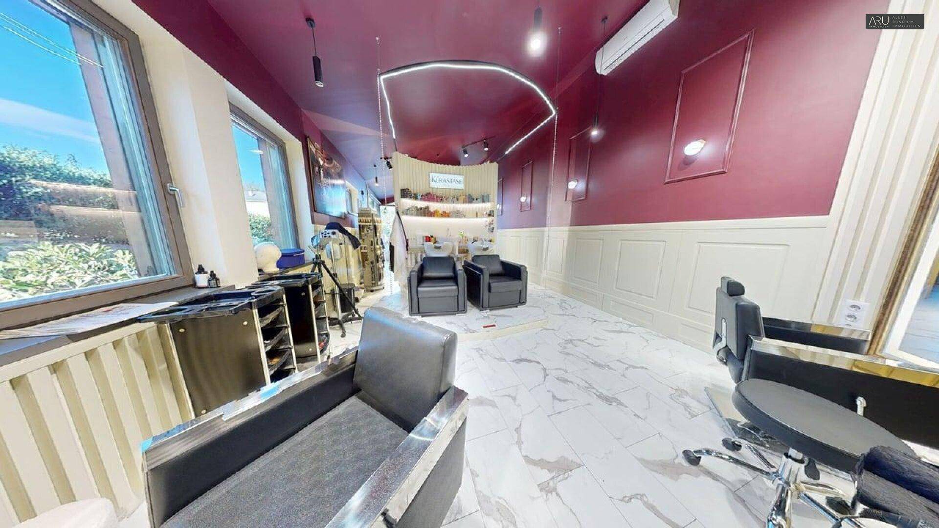 Wartebereich im Friseursalon mit bequemen Sesseln, großen Fenstern und Marmorboden.