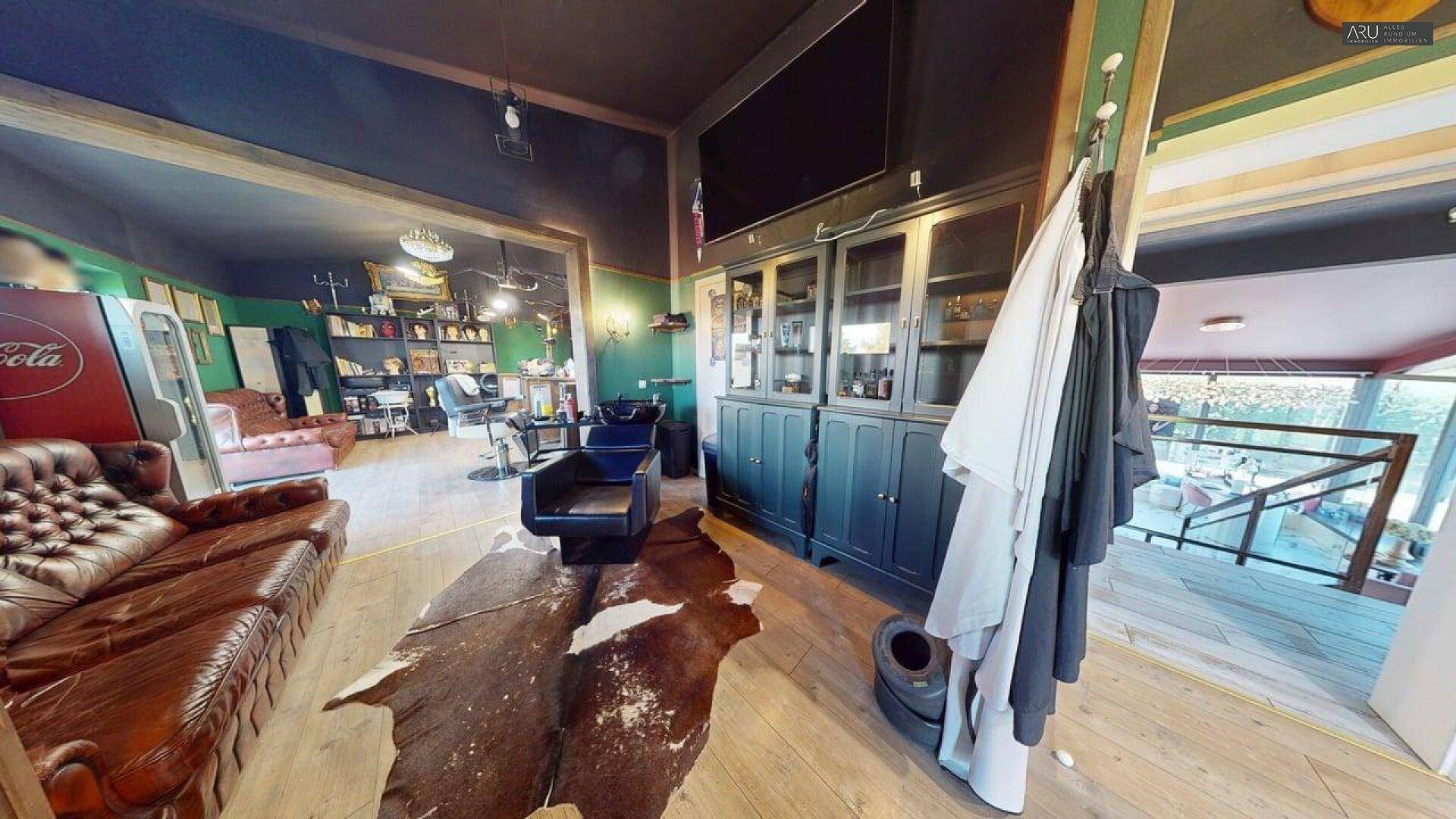 Lounge-Bereich im Barbershop mit Ledersofa, Kuhfellteppich und Holzfußboden.