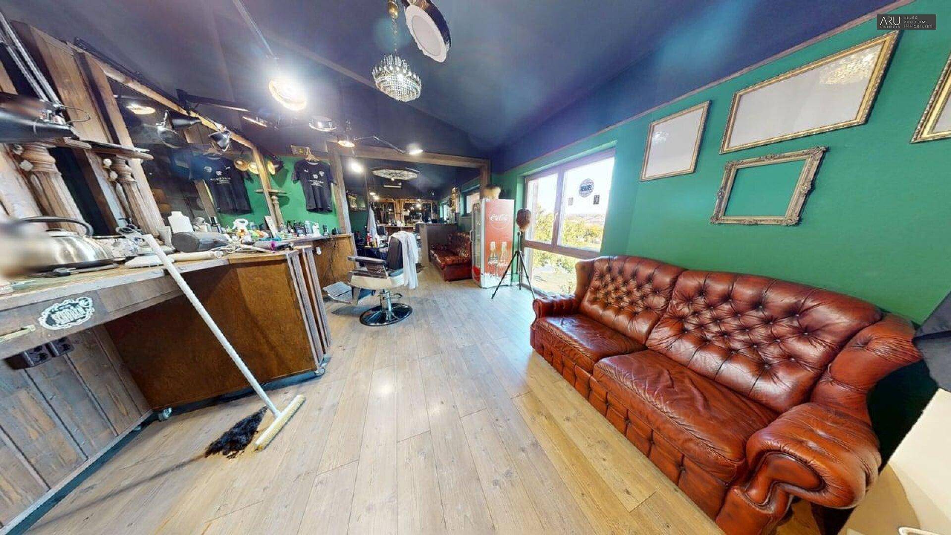 Gemütlicher Wartebereich im Barbershop mit Chesterfield-Sofa und Blick nach draußen.