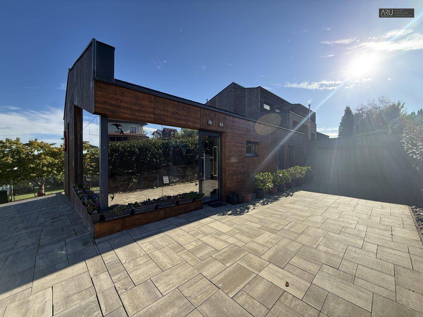 Rückansicht des modernen Gebäudes mit Holzfassade, großer Glasfront und gepflastertem Außenbereich.