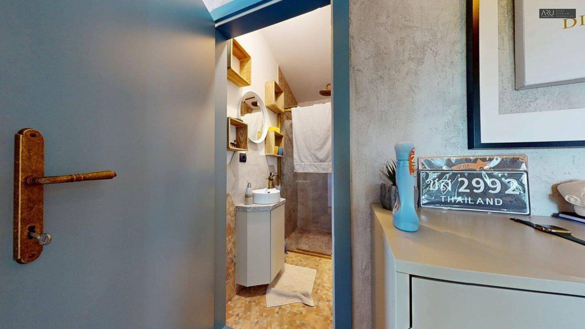Kleines Badezimmer mit modernem Waschbecken und Duschbereich, durch eine Tür sichtbar.