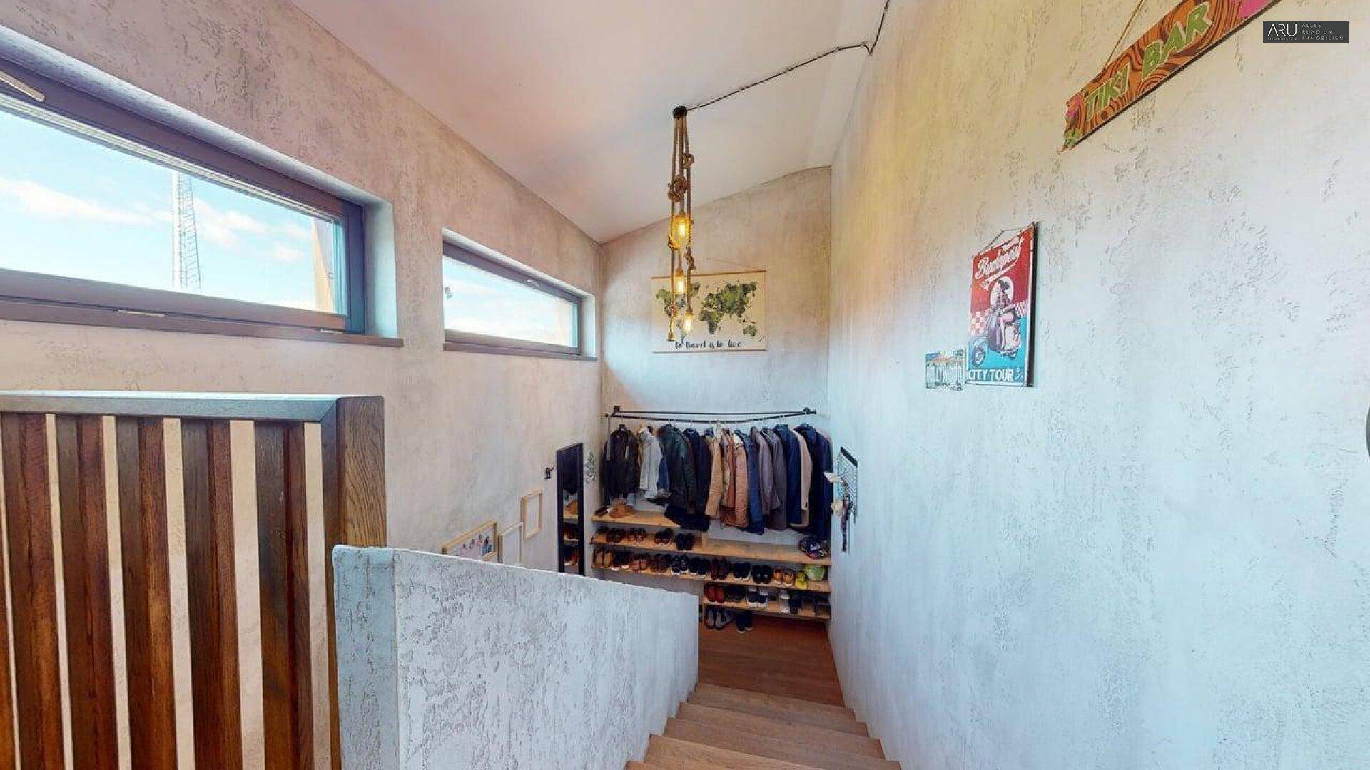 Heller Treppenbereich mit Fenstern und offener Garderobe für Kleidung und Schuhe.