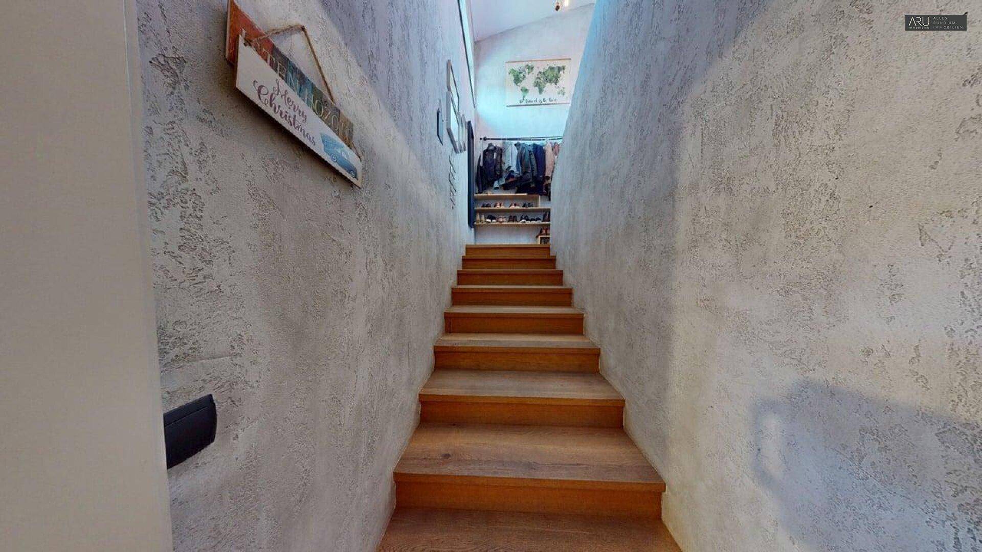 Treppenaufgang mit Holzstufen und strukturierten Wänden, führt zu einem offenen Bereich.