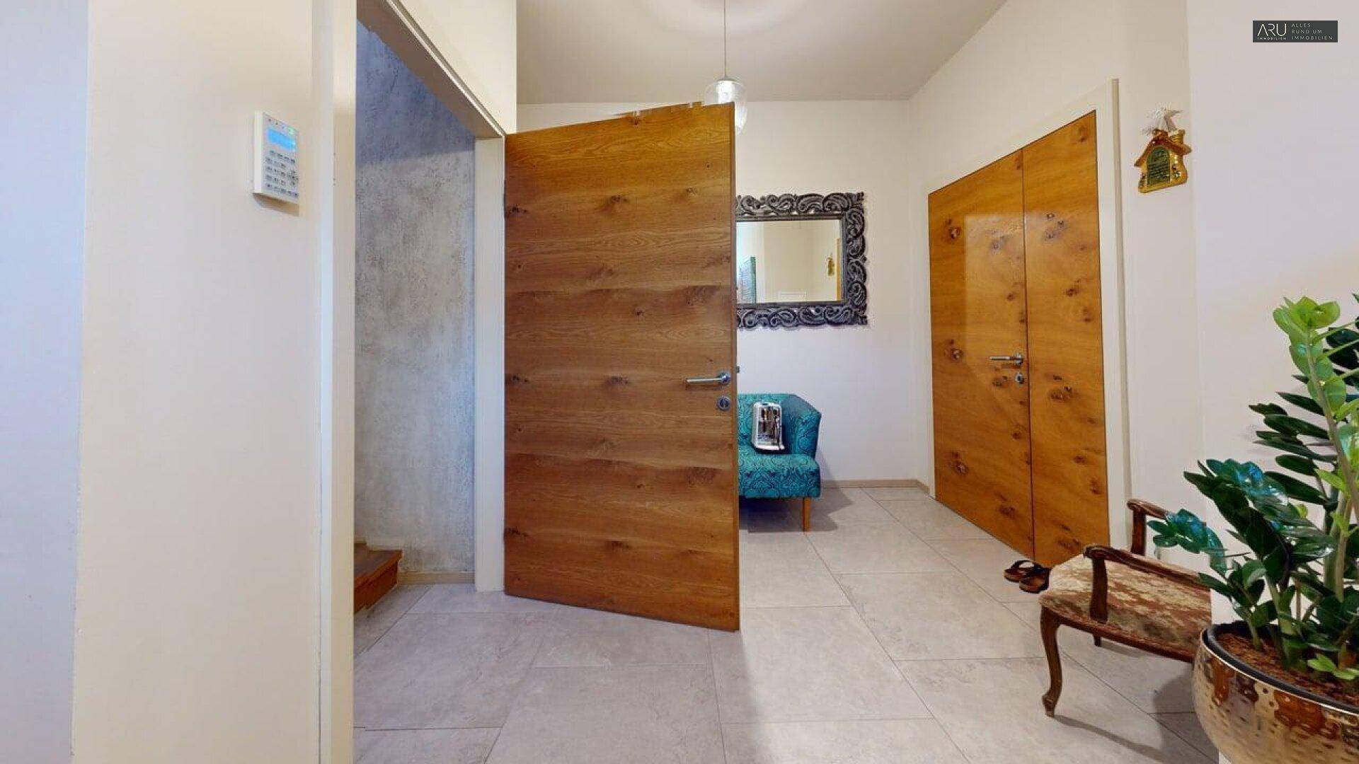 Heller Eingangsbereich mit Holztüren, Fliesenboden und dekorativer Sitzgelegenheit.