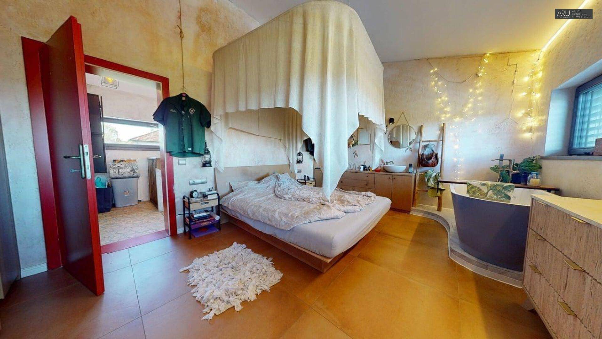 Schlafzimmer mit großem Bett, freistehender Badewanne und dekorativer Beleuchtung.