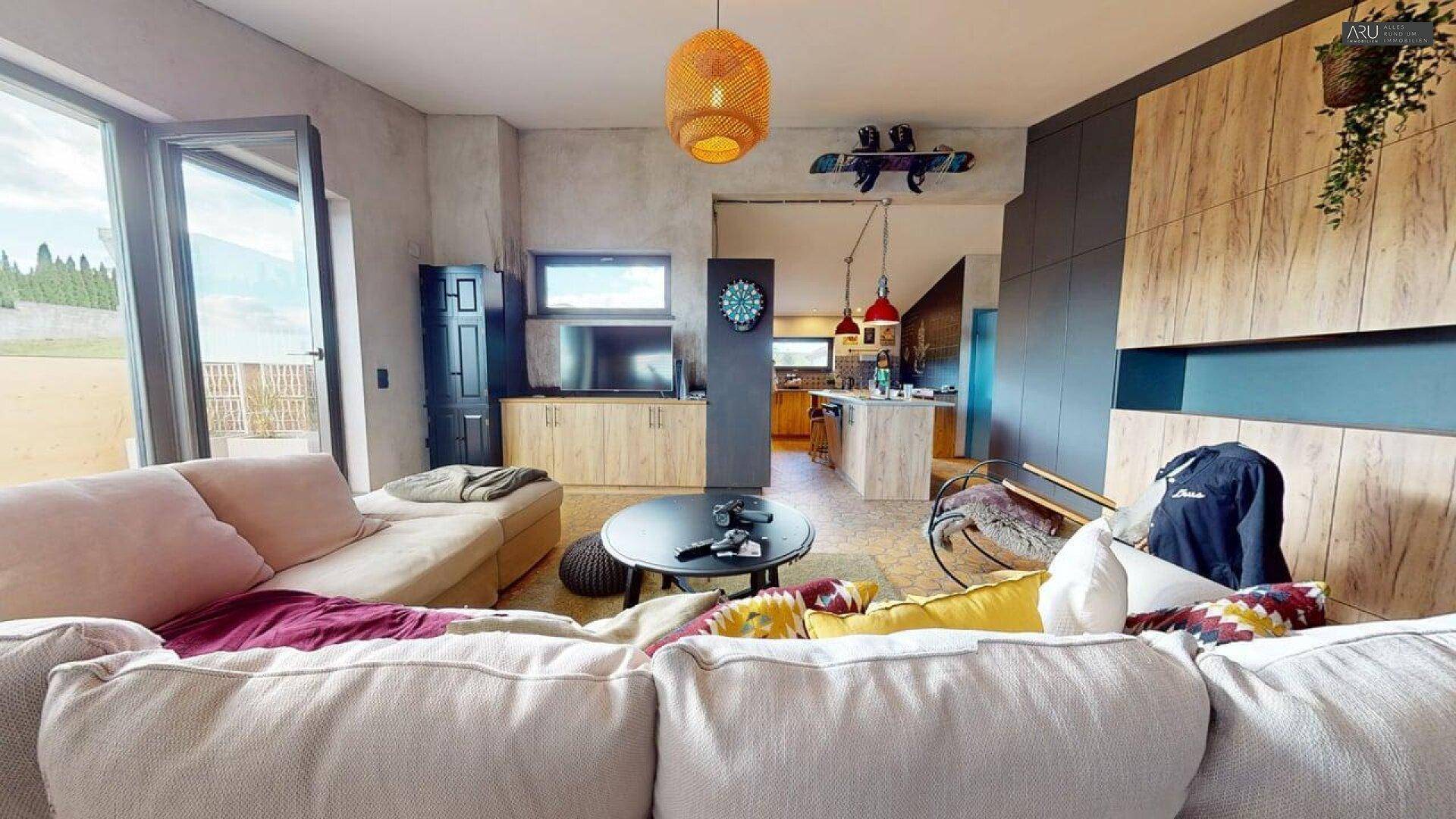 Offener Wohnbereich mit Sofa, Fernseher und Blick in die angrenzende Küche.