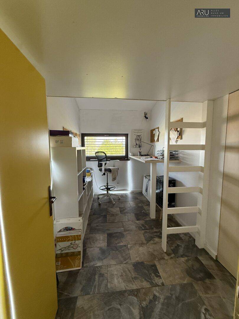 Arbeitszimmer mit Schreibtisch, Regalen und Leiter, bietet viel Stauraum.