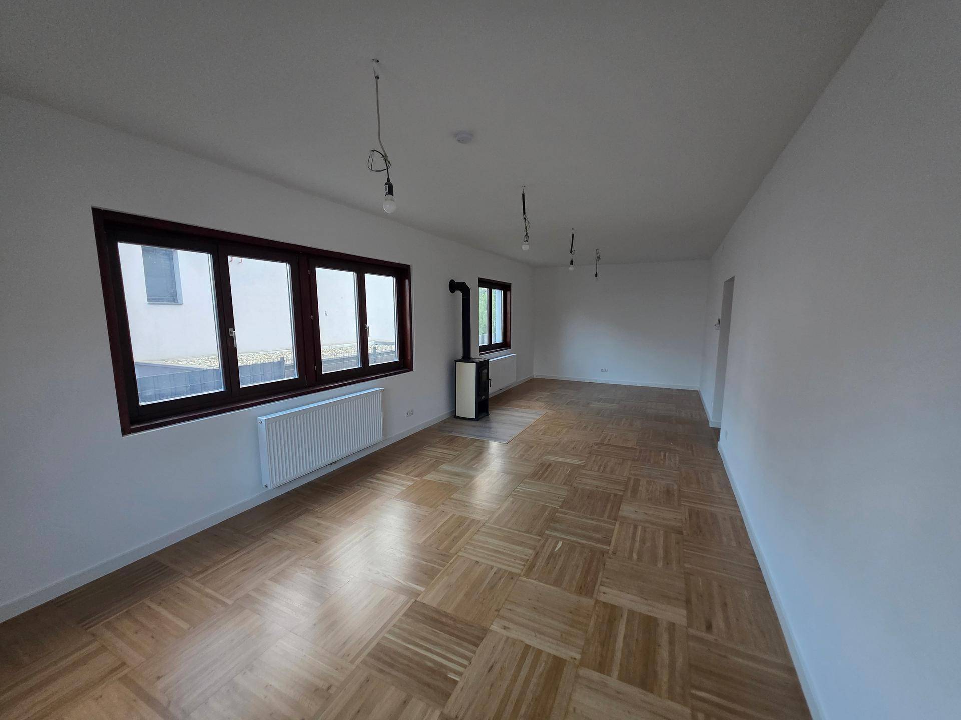 Helles Wohnzimmer mit Parkettboden, großen Fenstern und einem modernen Kaminofen.
