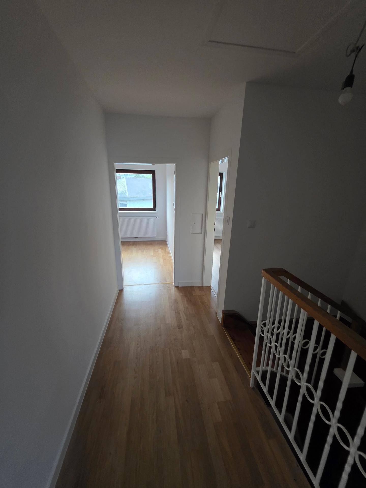 Heller Flur mit Holzfußboden und Treppenabgang, verbindet die verschiedenen Wohnbereiche.