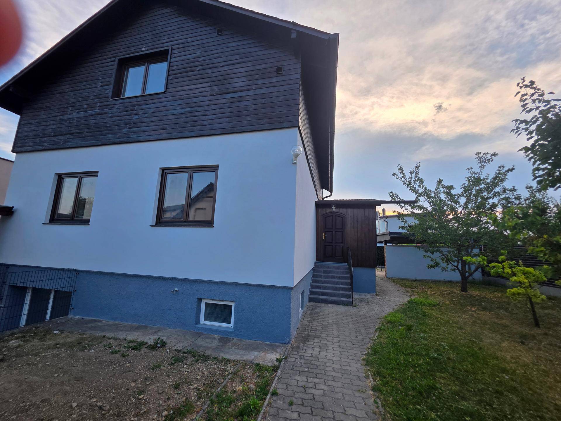 Ansicht des Einfamilienhauses mit weißer Fassade, dunklem Dach und gepflastertem Weg.