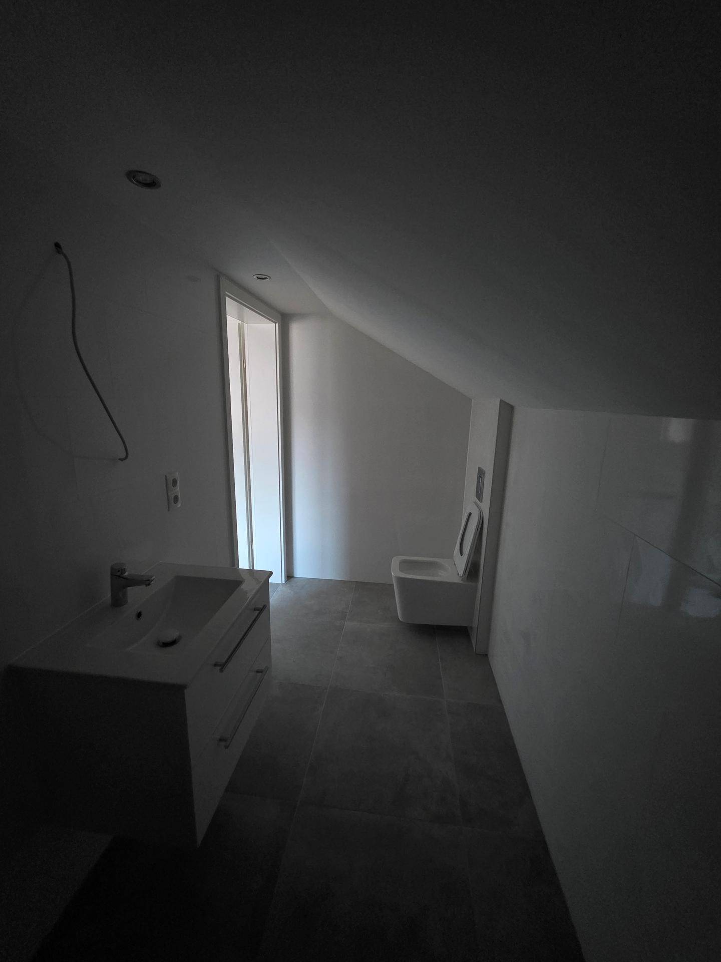 Modernes Badezimmer mit Waschtisch, wandhängendem WC und Fliesenboden im Dachgeschoss.